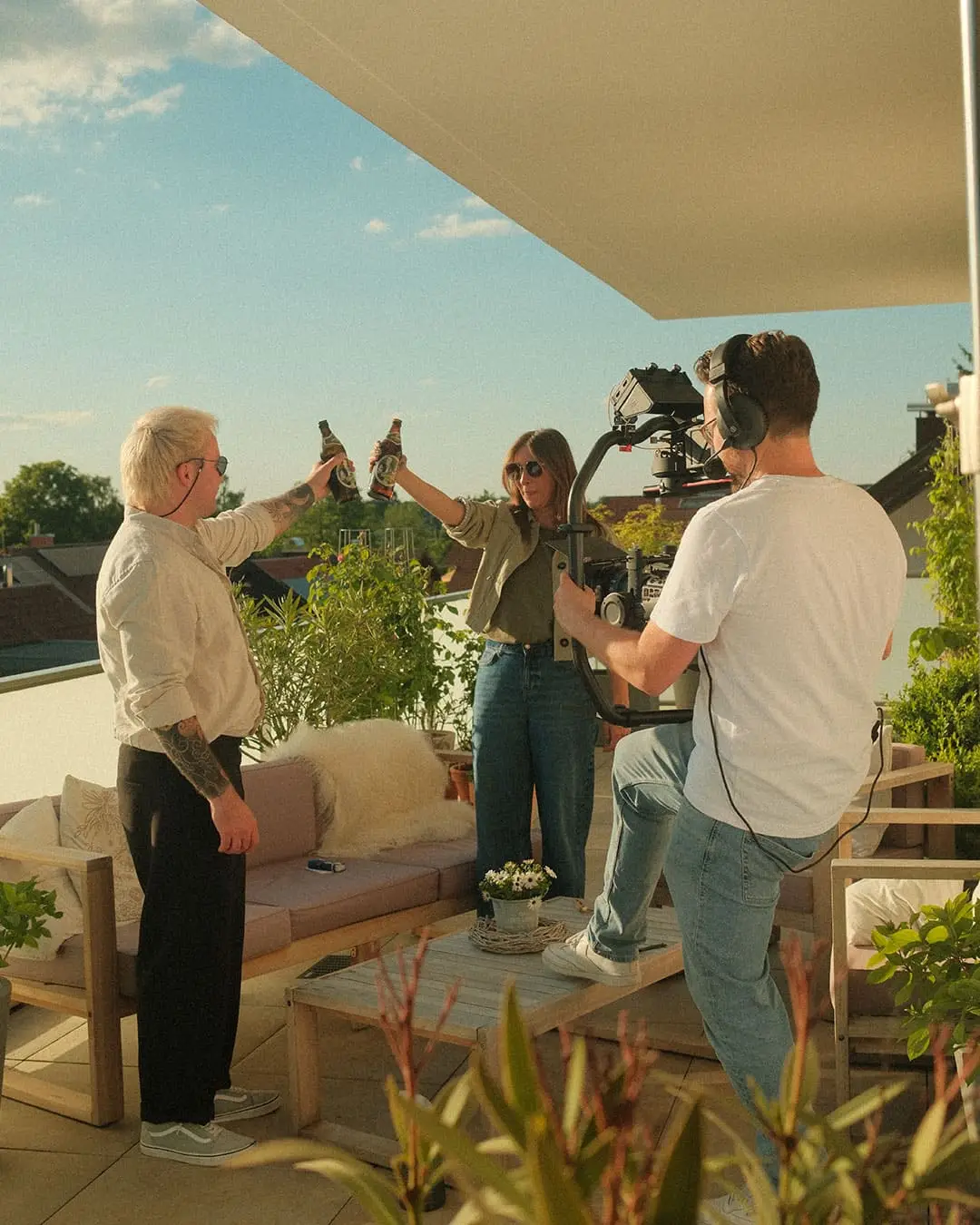 Filmteam dreht Werbeszene mit anstoßenden Flaschen auf sonniger Dachterrasse