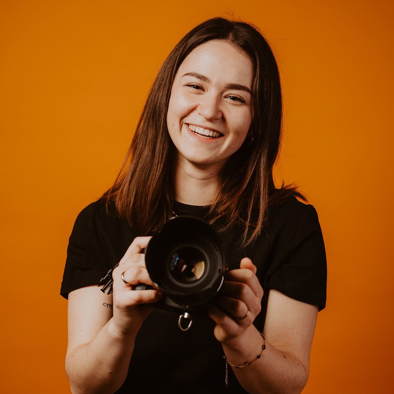 Fotografin mit Kamera vor orangefarbenem Hintergrund  goldencutmedia