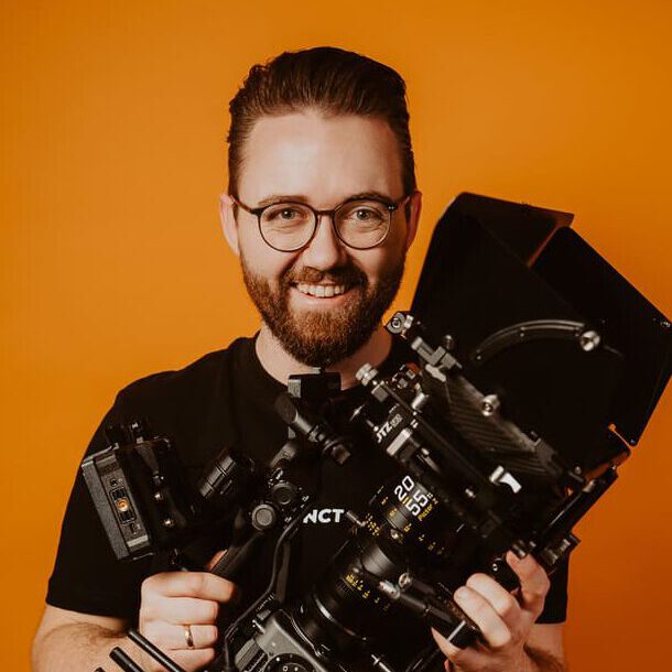 Kameramann mit professioneller Filmkamera vor orangefarbenem Hintergrund
