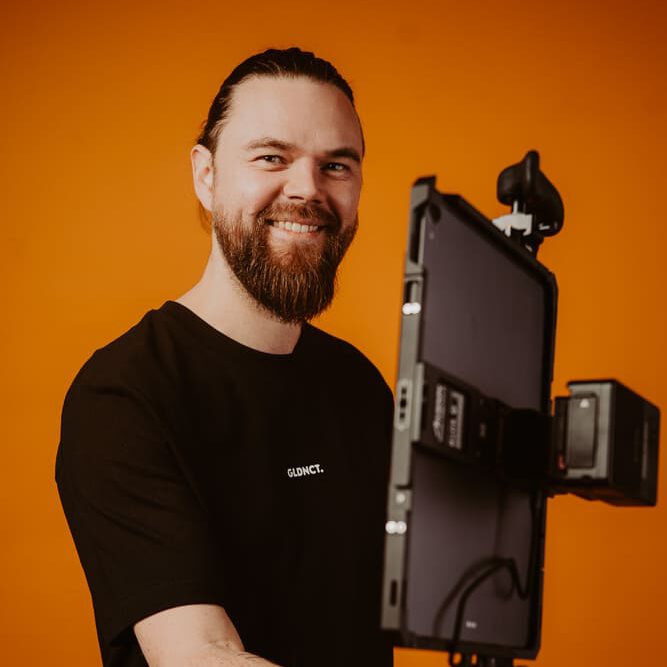 Kameramann mit professionellem Video Setup vor orangefarbenem Hintergrund